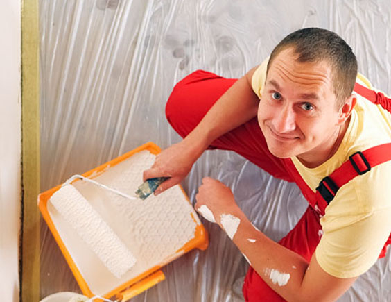 Pintor sonriendo mientas coge pintura con el rodillo