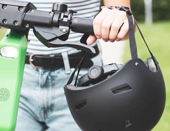 Persona circulando en patinete eléctrico con el casco de la mano