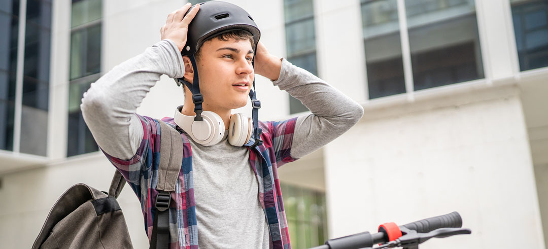 Chico estudiante poniendo el casco para circular en patinete eléctrico