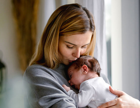 Mujer sosteniendo un bebé sobre sus brazos y apoyado en su pecho