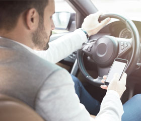 Joven con un mano en el volante y con el móvil en la otra mano